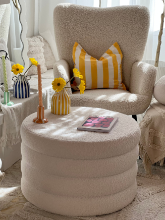Polsterhocker als Ablagefläche – praktisches Designmöbel im Color-Blocking-Look Gemütliche Leseecke mit cremefarbenem Sessel, rundem Polsterhocker und dekorativen Vasen im Clean-Living-Stil