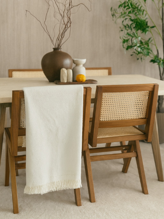 Esszimmer mit hellem Holztisch und St&uuml;hlen aus Holz mit Geflecht, dekoriert mit einer Vase und umgeben von gr&uuml;nen Pflanzen.