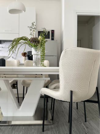 Helles Esszimmer mit wei&szlig;em Esstisch in V-Form, beigen Polsterst&uuml;hlen und dekorativer Vase mit gr&uuml;nen Pflanzen.