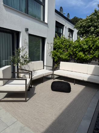 Komplette Terrasse mit moderner Gartenlounge, Outdoor-Teppich und gr&uuml;ner Pflanzenwand als nat&uuml;rlichem Sichtschutz
