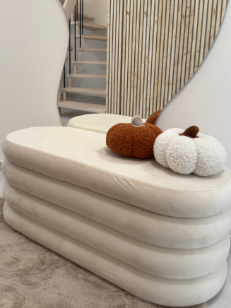 Weiche, gestufte Polsterbank in Creme mit flauschiger Deko in K&uuml;rbisform vor einer modernen Treppe.