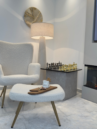 Gem&uuml;tliche Leseecke mit cremefarbenem Sessel, Hocker, Stehlampe und modernem Beistelltisch mit Schachbrett im Influencer-Interior.