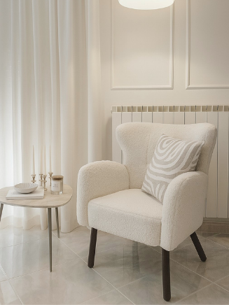 Beiger Sessel mit Kissen neben rundem Beistelltisch im hellen, minimalistischen Raum