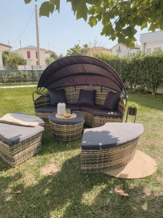 Runde Polyrattan-Lounge mit Sonnenverdeck, grauen Auflagen und passendem Hocker auf einer Rasenfl&auml;che im Garten