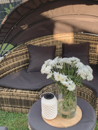 Detailansicht einer runden Polyrattan-Gartenlounge mit grauen Sitzkissen, Beistelltisch und Blumenvase