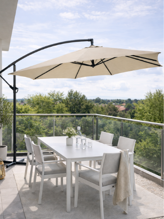 Moderner Balkon mit beigem Ampelschirm &uuml;ber wei&szlig;er Sitzgruppe und Blick ins Gr&uuml;ne