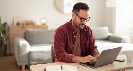 Mann mit Brille arbeitet konzentriert am Laptop in einem wohnlichen Umfeld &ndash; steht f&uuml;r Homeoffice oder mobiles Arbeiten