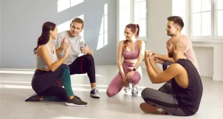 F&uuml;nf sportlich gekleidete Menschen sitzen in Sporthalle und unterhalten sich &ndash; steht f&uuml;r Firmenfitness oder Gemeinschaft