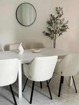 Modernes Esszimmer mit wei&szlig;em Esstisch, gepolsterten St&uuml;hlen in Creme und stilvollem Wandspiegel im minimalistischen Design.