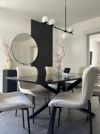 Modernes Esszimmer mit schwarzem Esstisch, hellen Polsterst&uuml;hlen und rundem Wandspiegel im minimalistischen Design.