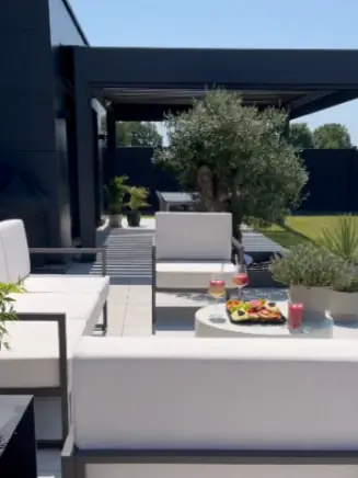 Outdoor-Loungebereich unter Pergola mit Sitzm&ouml;beln und Tisch mit Snacks und Getr&auml;nken.