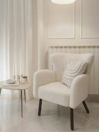 Beiger Sessel mit Kissen neben rundem Beistelltisch im hellen, minimalistischen Raum