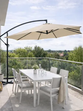 Moderner Balkon mit beigem Ampelschirm &uuml;ber wei&szlig;er Sitzgruppe und Blick ins Gr&uuml;ne